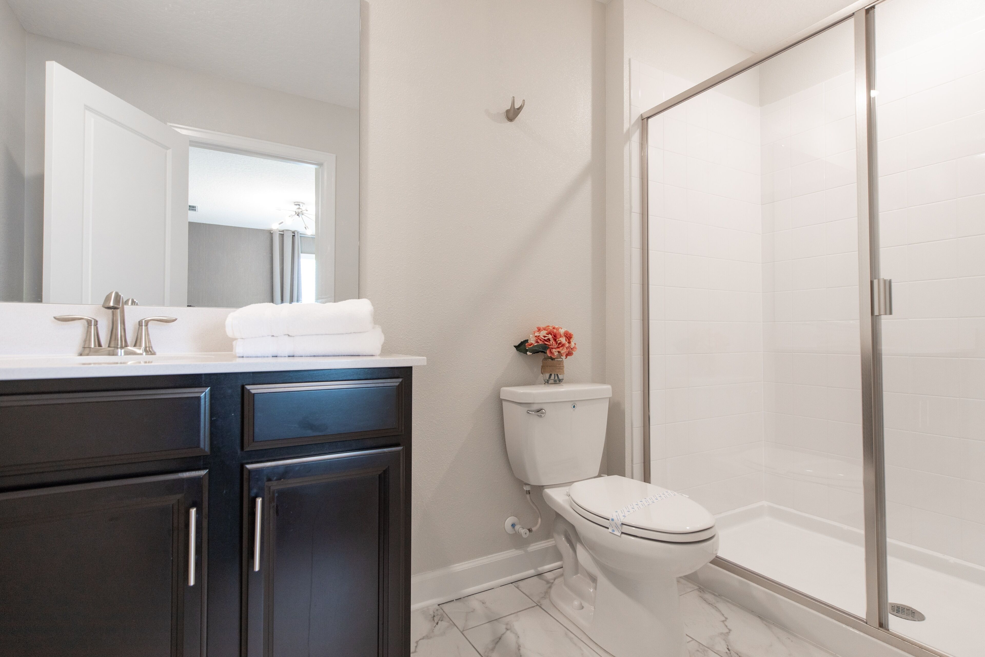 A modern bathroom with a white toilet, a glass shower enclosure, and dark cabinetry.