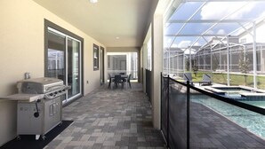 Une terrasse extérieure couverte équipée d’un barbecue, d’un coin repas et d’une piscine.