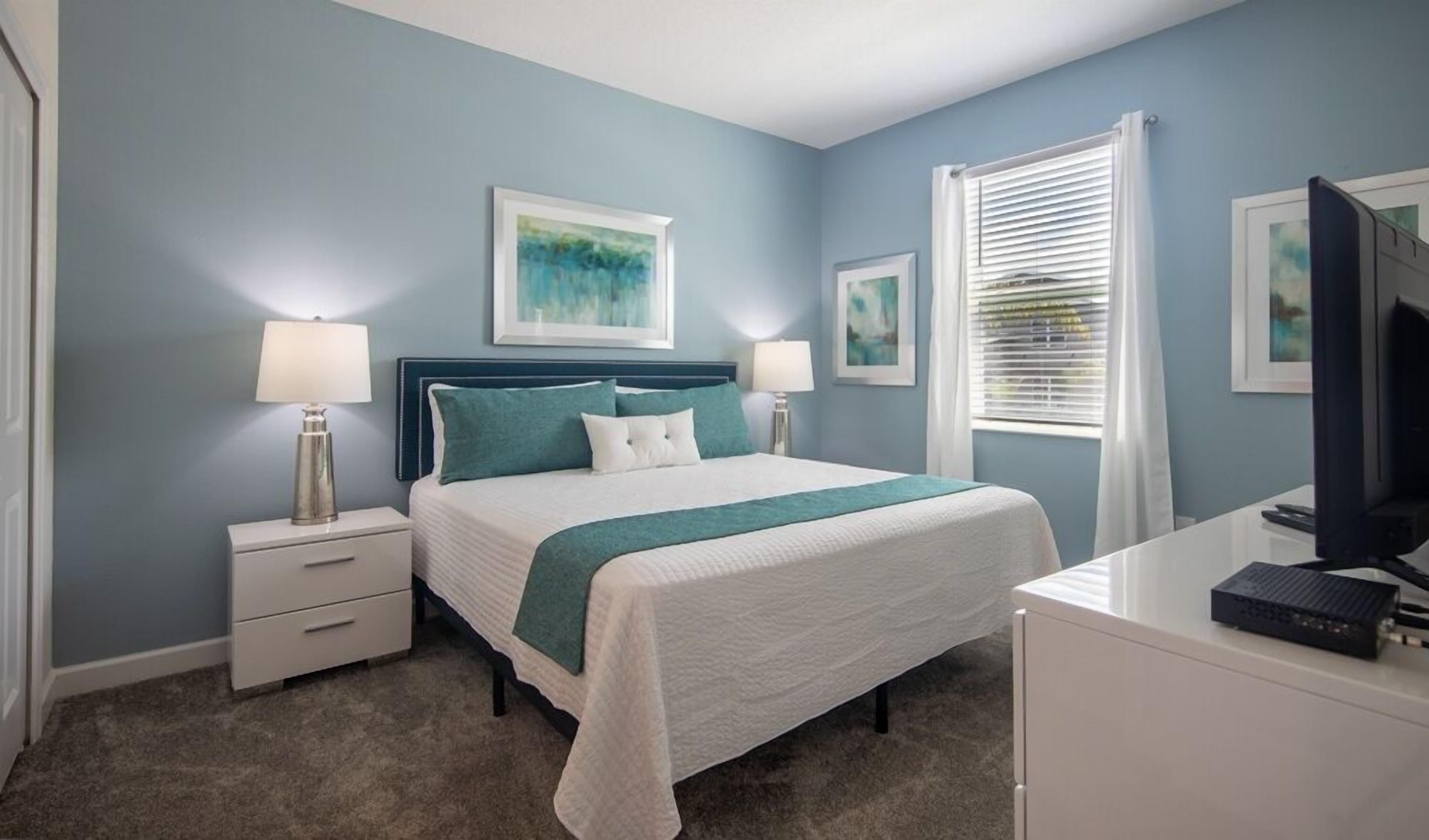 A bedroom with a bed, nightstands, a desk, and a television.