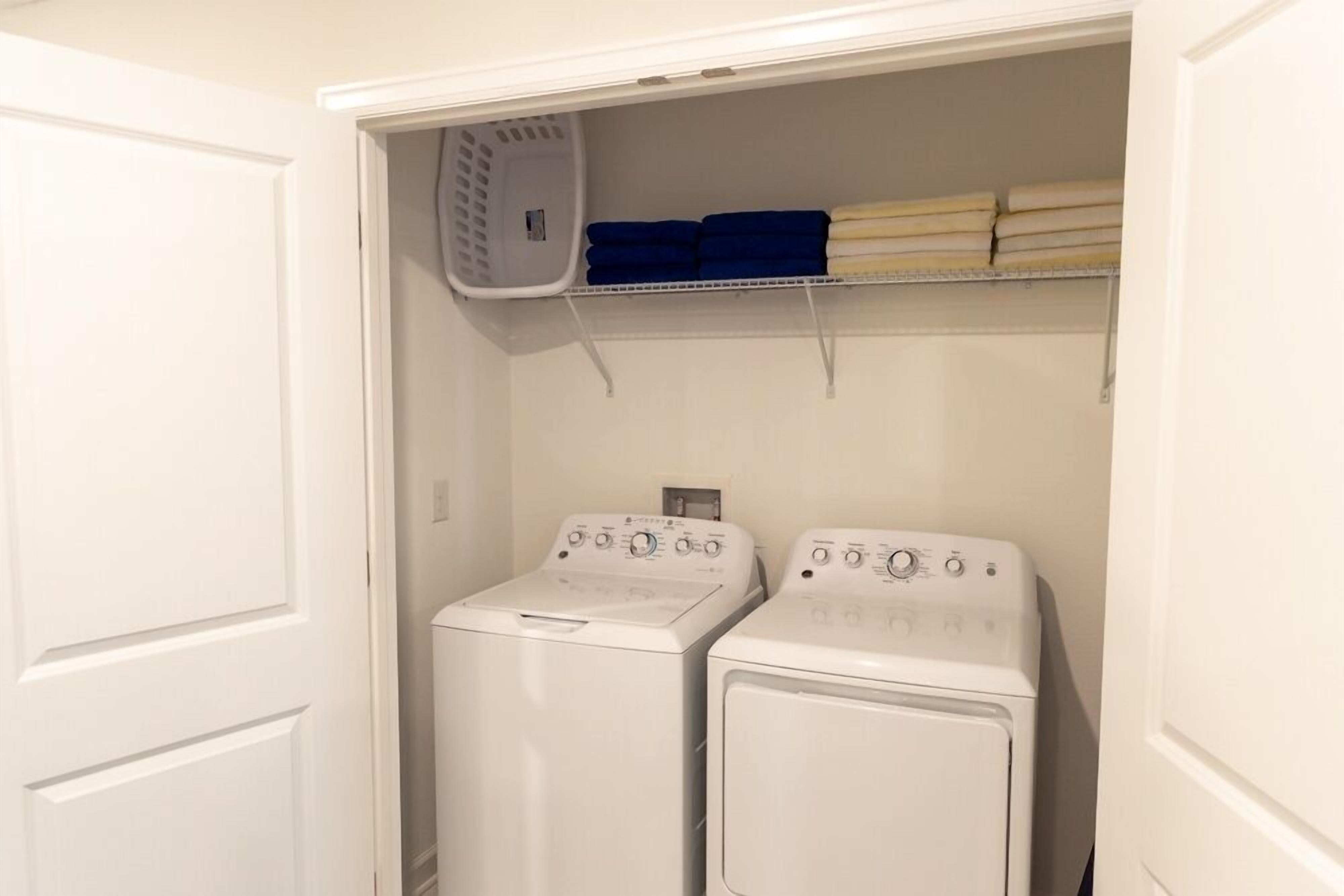 A laundry area with two white front-loading washing machines and a shelf above holding folded towels.