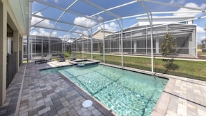 Une piscine extérieure couverte, dotée d’une structure en verre, de chaises longues et d’un petit jacuzzi.