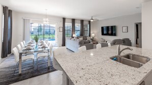 A modern kitchen with a granite countertop, stainless steel sink, and a dining area with a glass table and white chairs. - 7547oml-solterra Resort 6 Bedroom Home by RedAwning (Davenport)