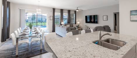 A modern kitchen with a granite countertop, stainless steel sink, and a dining area with a glass table and white chairs.