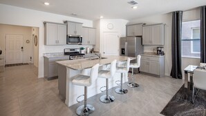 A modern kitchen with a central island, stainless steel appliances, and white bar stools. - 7547oml-solterra Resort 6 Bedroom Home by RedAwning (Davenport)