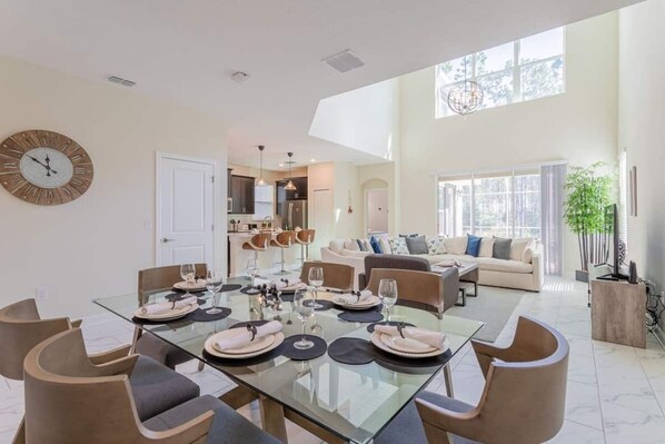 A spacious living area with a glass dining table set for six, a sofa, and a large window offering a view of the outdoors.