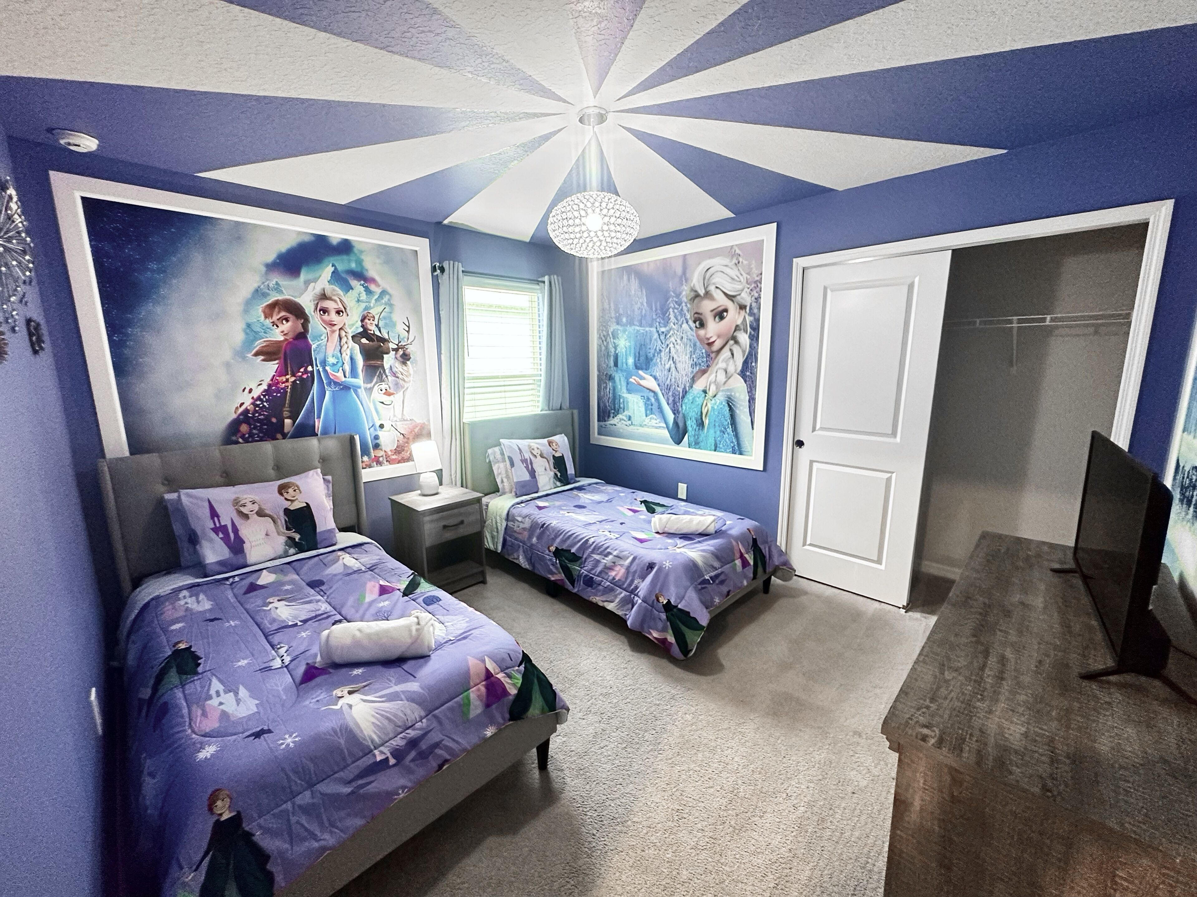 A bedroom with two beds, a chandelier, and posters of animated characters.