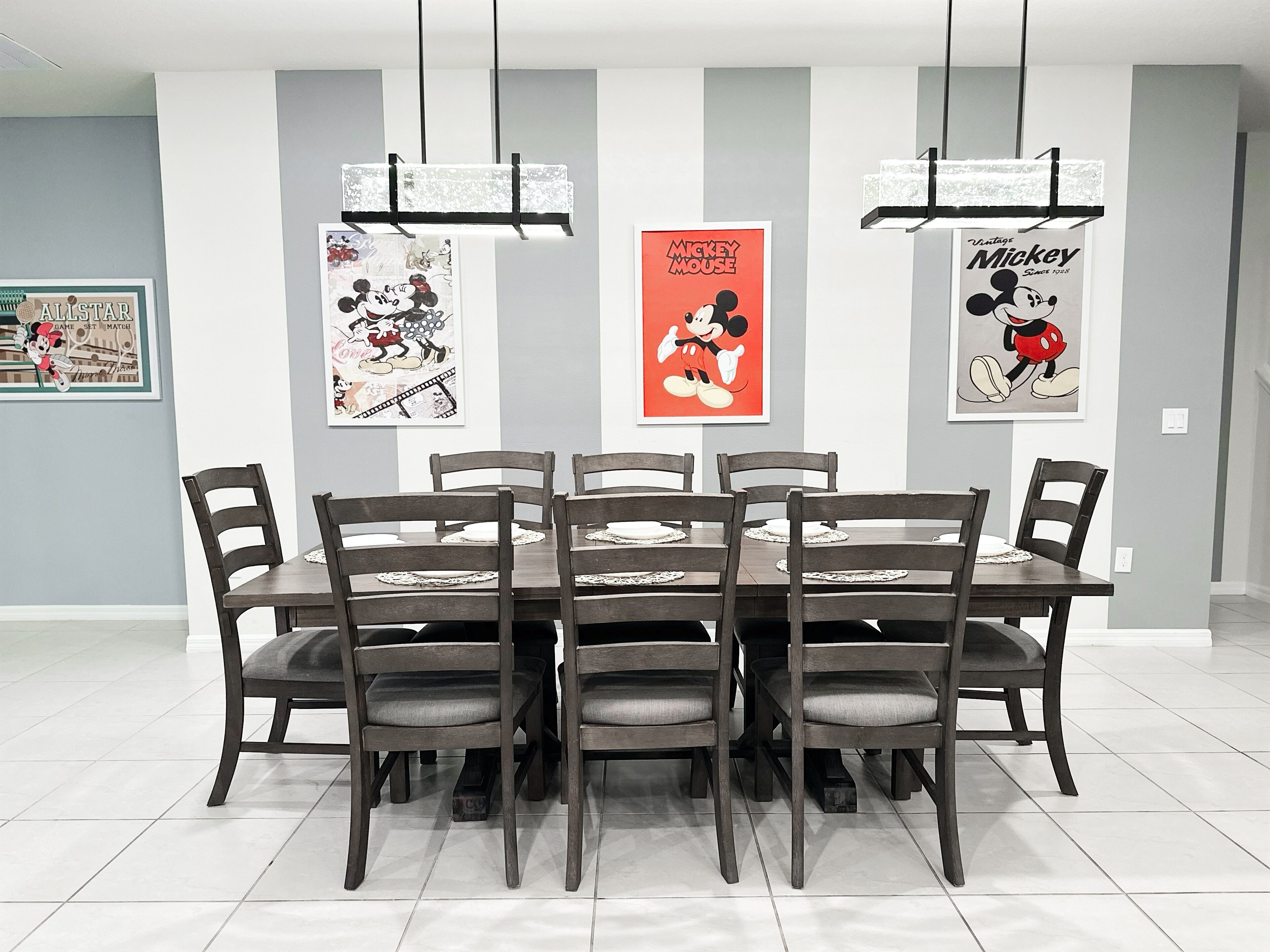 Een eethoek met een rechthoekige tafel, omringd door zes stoelen, drie hangende吊灯 en drie ingelijste posters aan de wand.