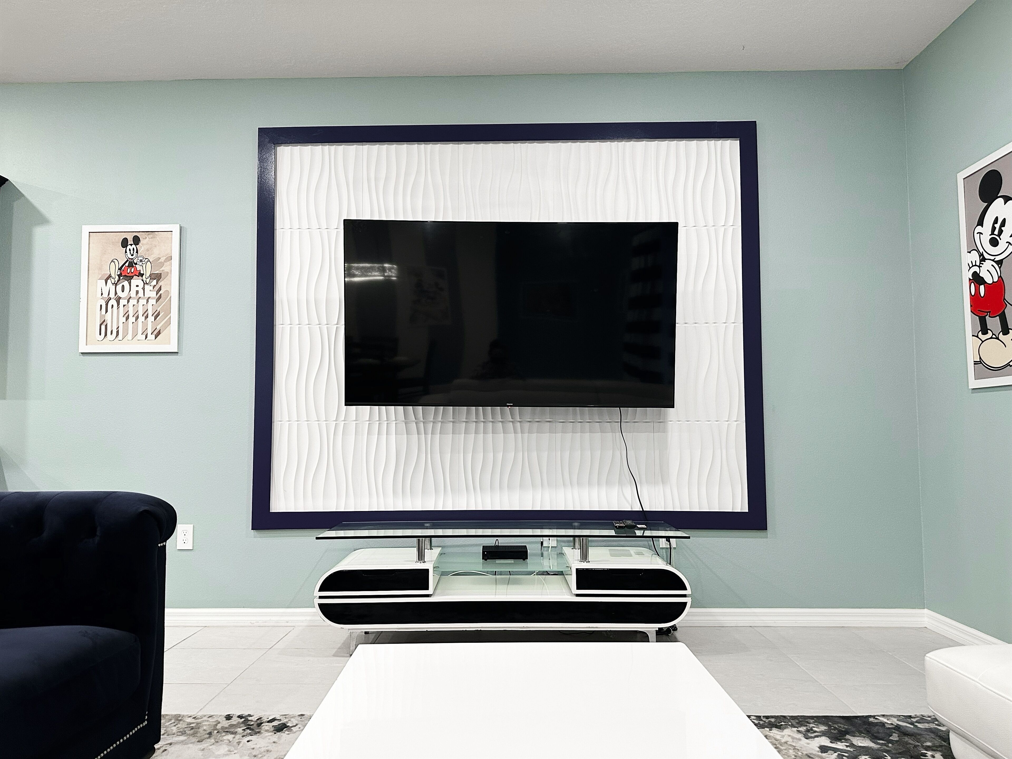 Ein Wohnzimmer mit Flachbildfernseher an der Wand, einem dunkelgrauen Sofa und einem weißen Couchtisch.