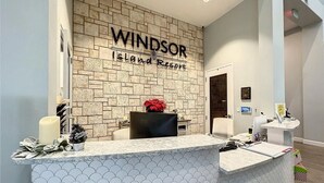 A reception desk at Windsor Island Resort with a brick wall backdrop, a potted plant, and a mirror above the counter. - 2127lc- Windsor Island 10 Bedroom Home by RedAwning (Davenport)