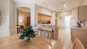 A modern kitchen with wooden cabinets, a central island, and a dining area with a wooden table and chairs. - 246bd-highlands Reserve 4 Bedroom Home by RedAwning (Davenport)