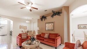 A spacious living room with a ceiling fan, a red sofa, a coffee table, and decorative plants. - 246bd-highlands Reserve 4 Bedroom Home by RedAwning (Davenport)