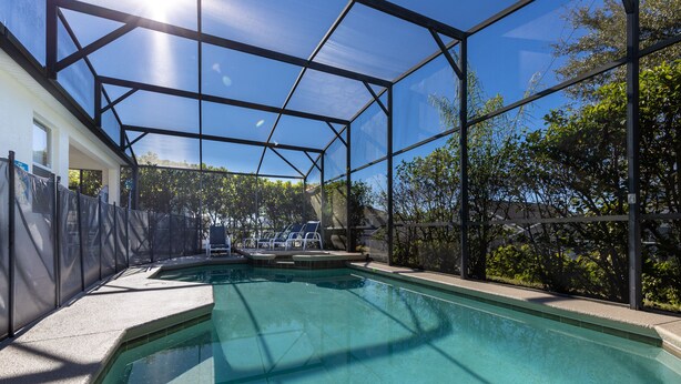A swimming pool with a glass enclosure, surrounded by a fence and trees. - 246bd-highlands Reserve 4 Bedroom Home by RedAwning (Davenport)