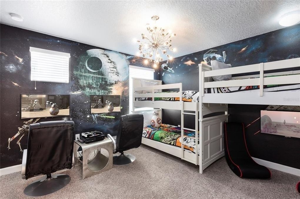 Une chambre avec des lits superposés, un bureau et une chaise, décorée avec des œuvres d’art murales sur le thème de l’espace et agrémentée d’un lustre.