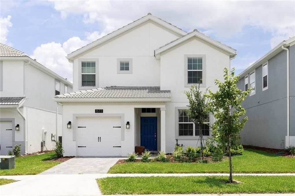 A two-story residential building with a white exterior, a blue front door, and a garage.