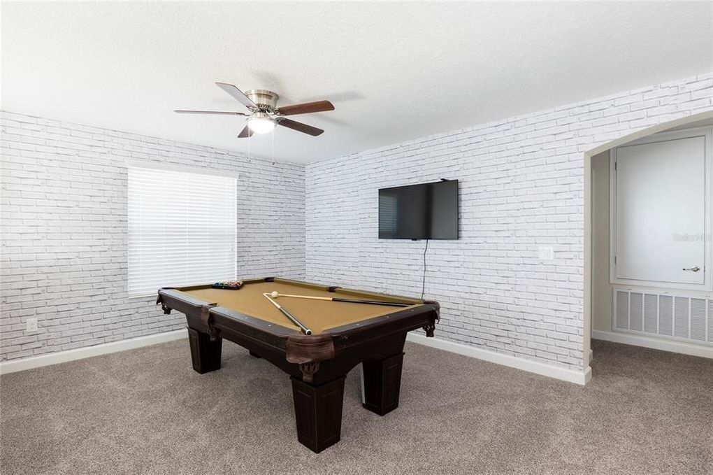 A room with a pool table, a ceiling fan, a TV mounted on the wall, and a door.