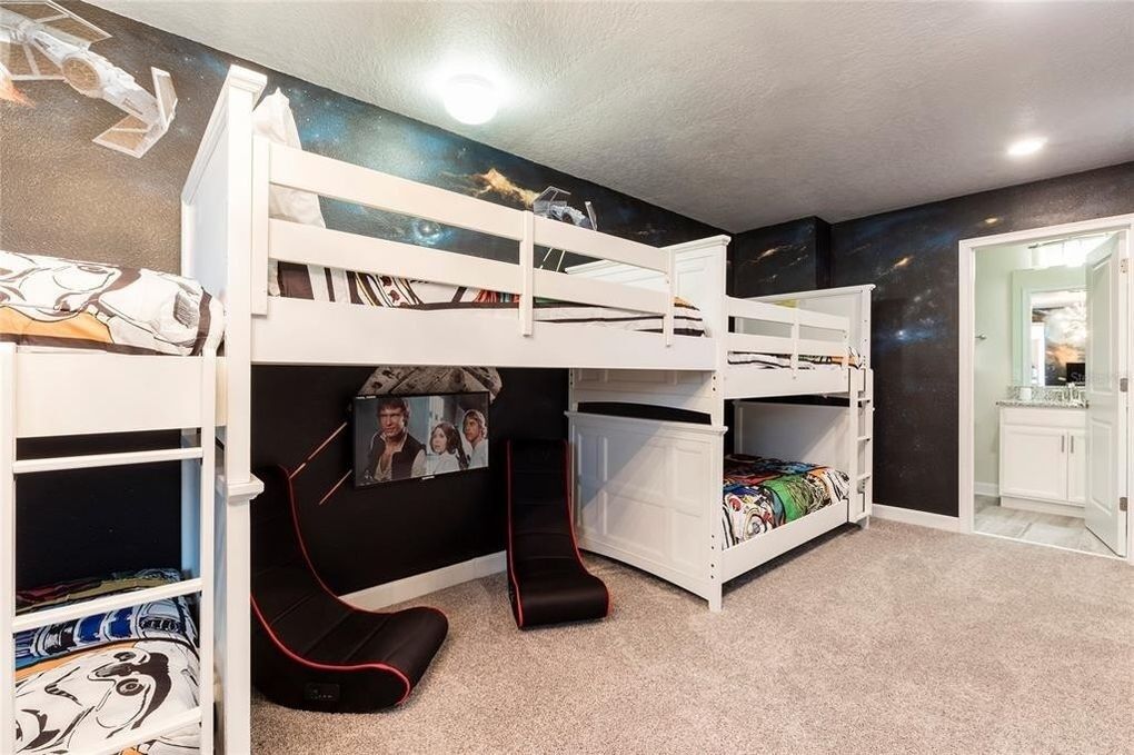 A bunk bed room with a galaxy-themed wall mural, a white door, and a small kitchenette area.