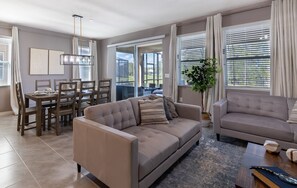 A modern living room with a sofa, a dining table, and a large window with blinds.