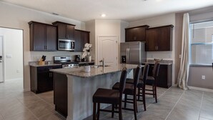 A modern kitchen with dark wood cabinets, stainless steel appliances, and a large island with bar stools. - 7660oml-solterra Resort 5 Bedroom Home by RedAwning (Davenport)