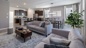 A modern living room with a grey sofa, a coffee table, and a dining area with a table and chairs. - 7660oml-solterra Resort 5 Bedroom Home by RedAwning (Davenport)