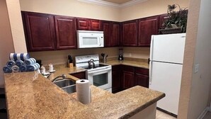 Una cocina con armarios de madera oscura, un refrigerador blanco, una estufa y un microondas.