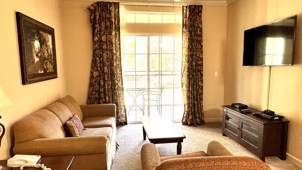 A living room with a sofa, armchair, coffee table, and a TV on a stand. - 1301tt Unit 9108- Tuscana Resort 3 Bedroom Condo by RedAwning (Davenport)