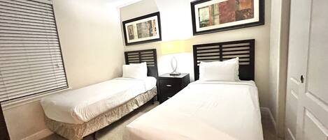 A hotel room with two single beds, a nightstand with a lamp, and two framed pictures on the wall.