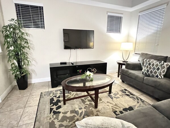 A living room with a flat-screen TV, a coffee table, a sofa, and a potted plant.