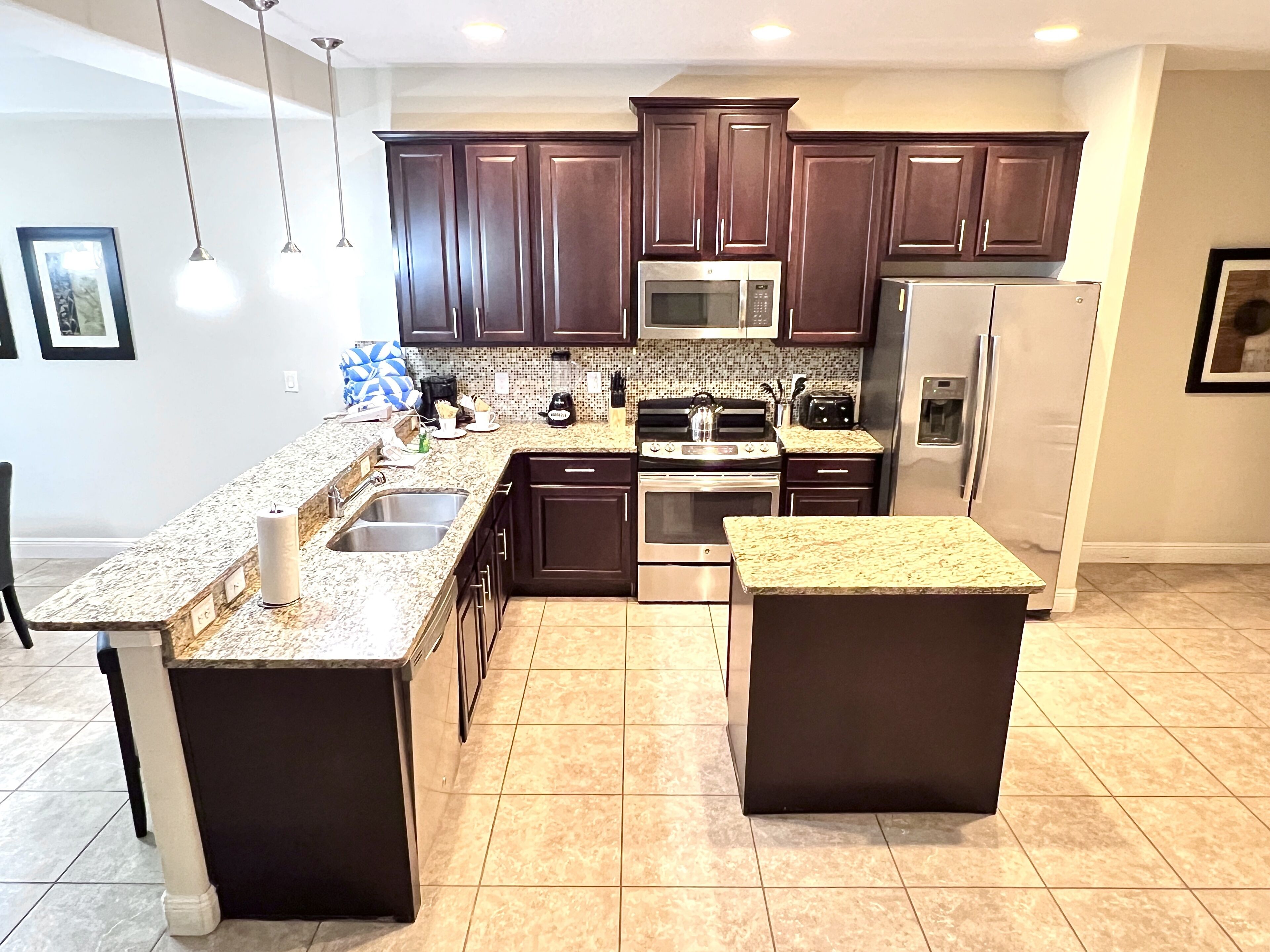 A modern kitchen with dark brown cabinets, stainless steel appliances, granite countertops, and a tiled floor.