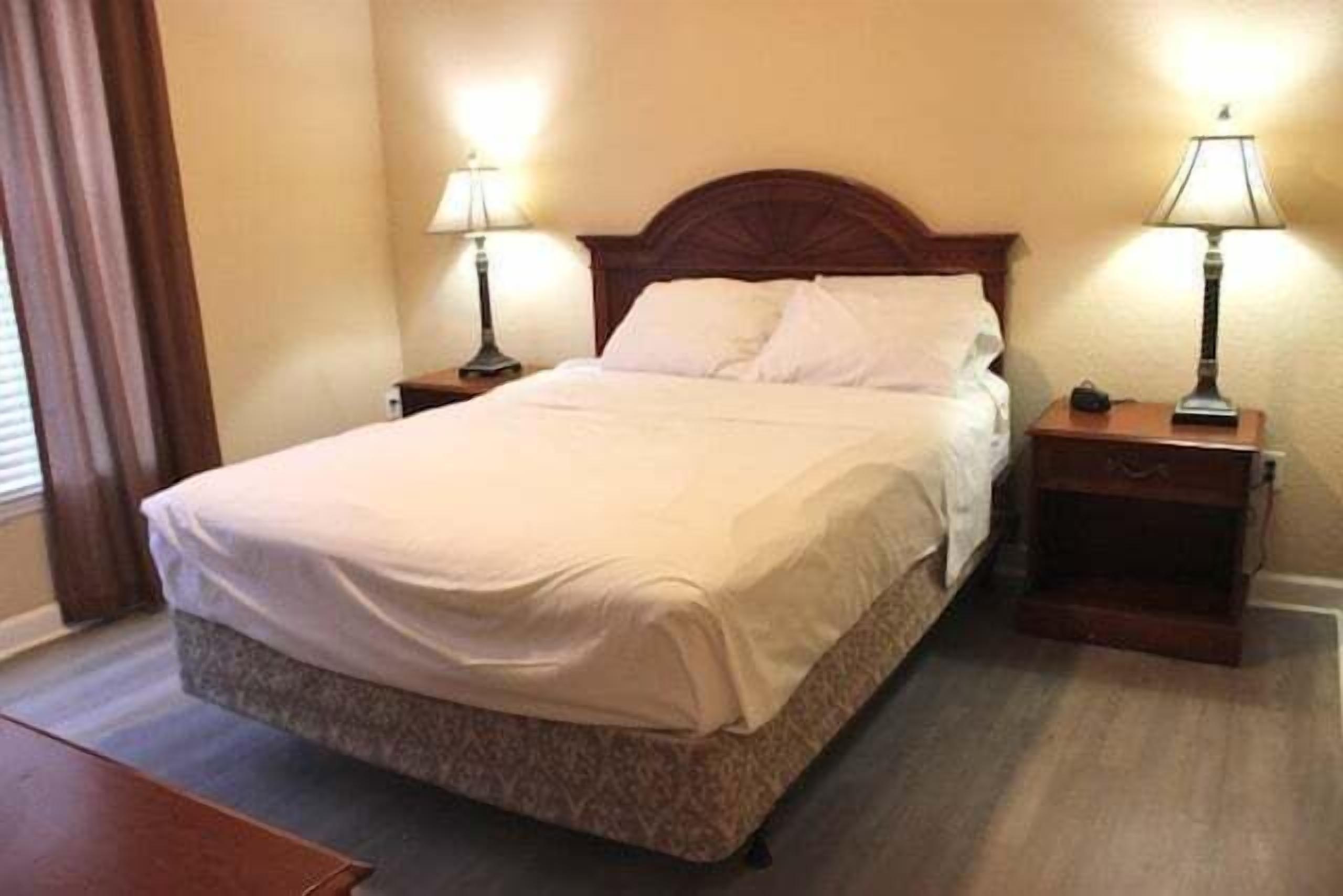A neatly made bed with a wooden headboard, two bedside tables with lamps, and a wooden nightstand.