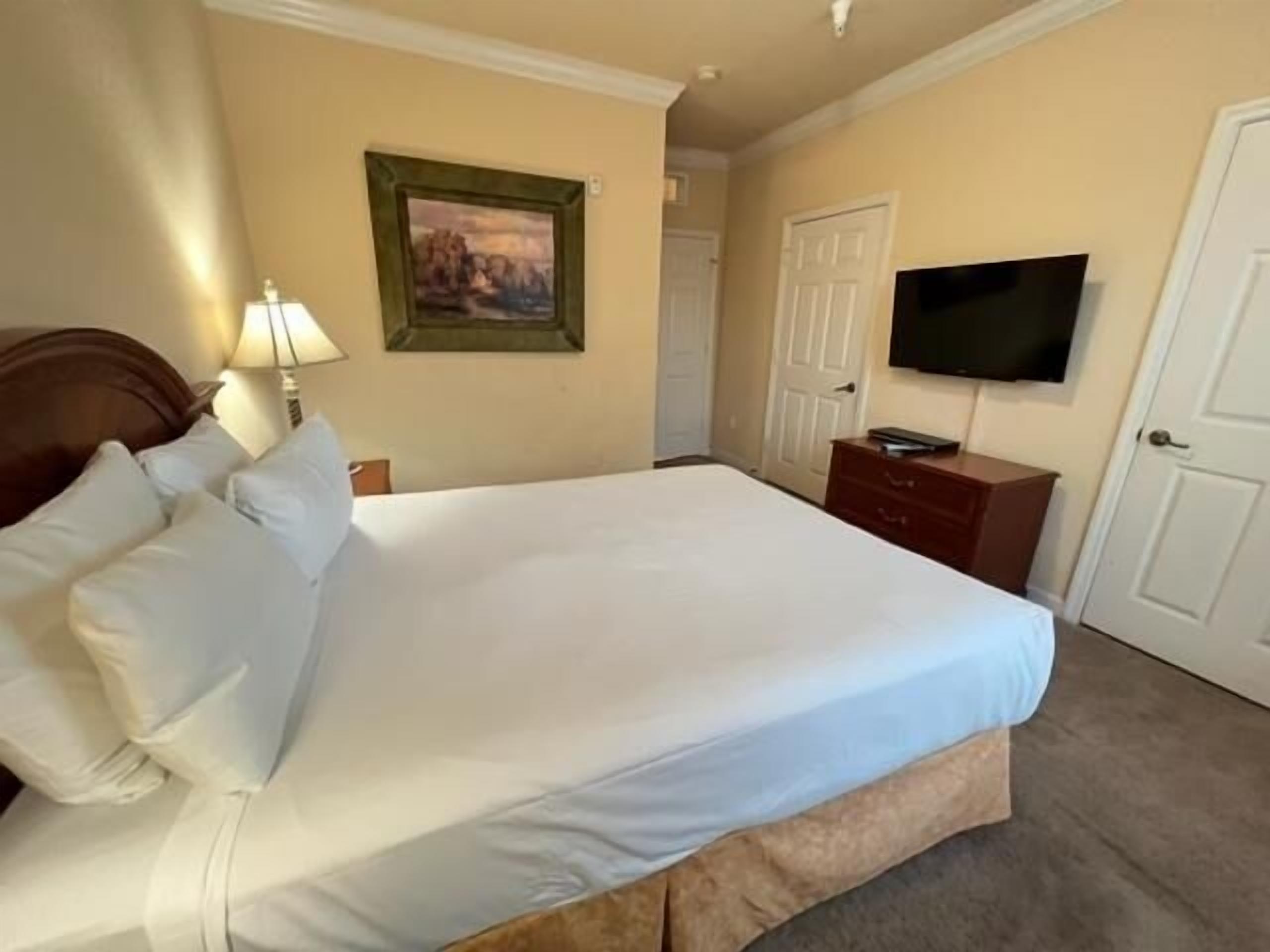 Quarto de hotel com uma cama grande, televisão na parede e uma porta.