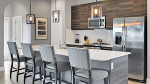 Une cuisine moderne dotée d’un îlot central, de tabourets de bar, d’appareils électroménagers en acier inoxydable et de meubles de rangement en bois.