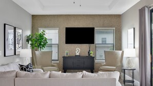Un salon moderne avec un canapé beige, deux fauteuils, un meuble de rangement noir pour appareils électroniques et un grand téléviseur à écran plat fixé à un mur à texture.
