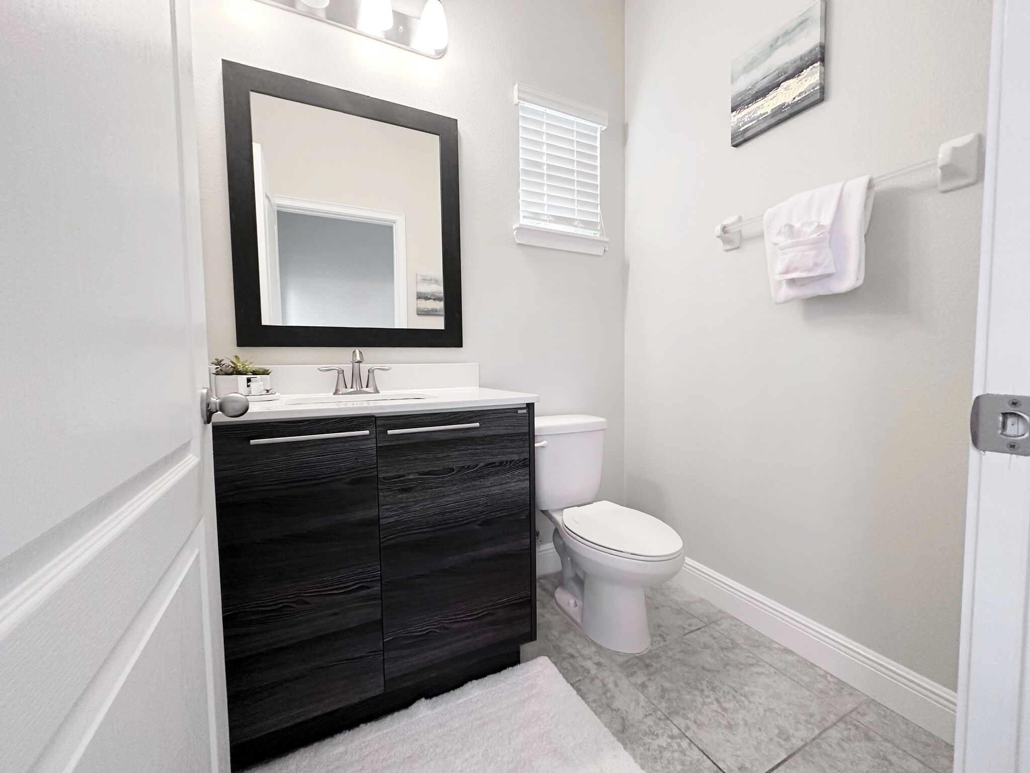 A modern bathroom with a dark wood vanity, white toilet, and a large mirror.