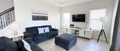 Ein modernes Wohnzimmer mit einem dunklen Sofa, einem weißen Konsolentisch, einem Flachbildfernseher und einer Lampe.