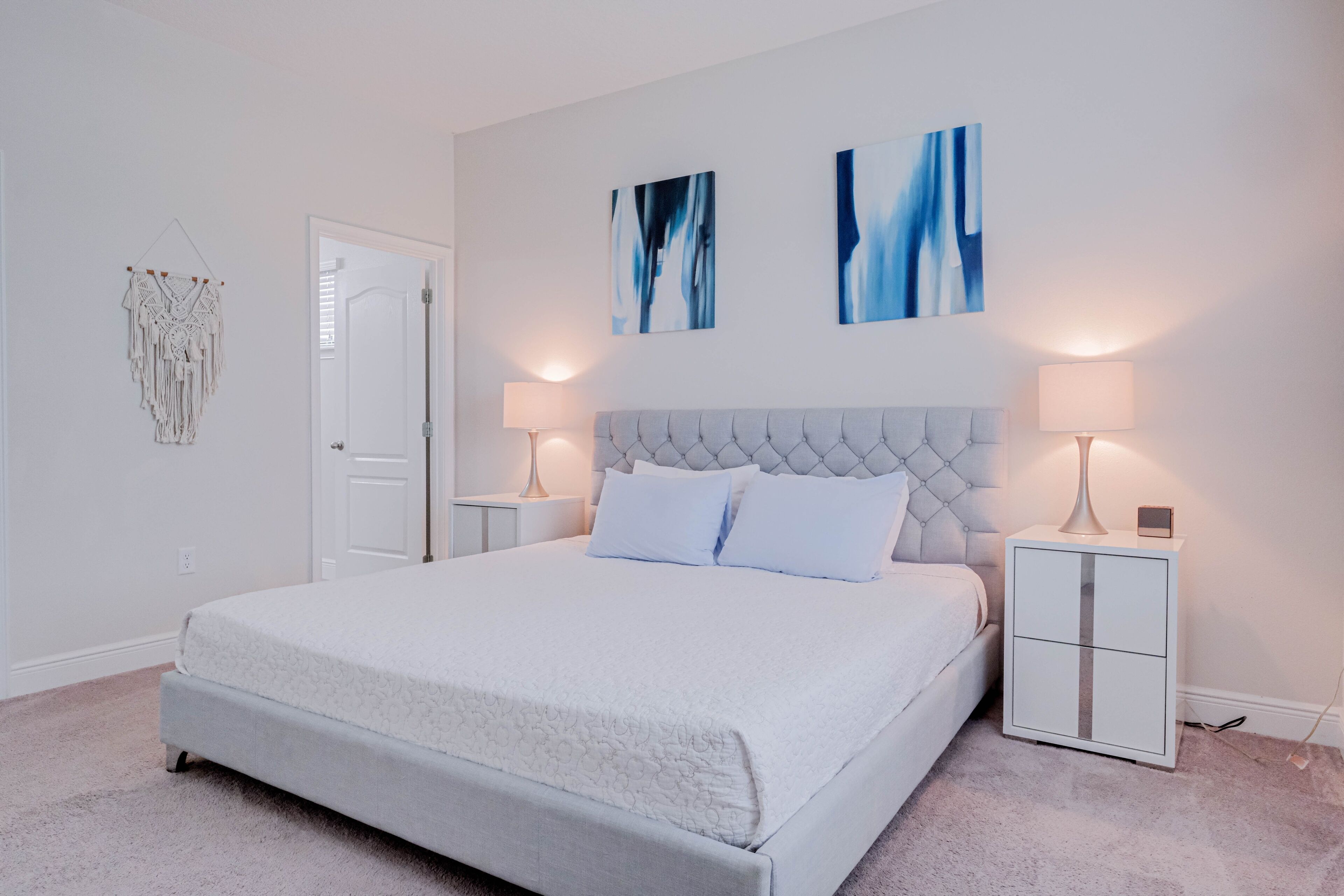 Um quarto com uma cama grande, duas mesas de cabeceira, um painel de cabeceira branco e arte abstrata na parede.