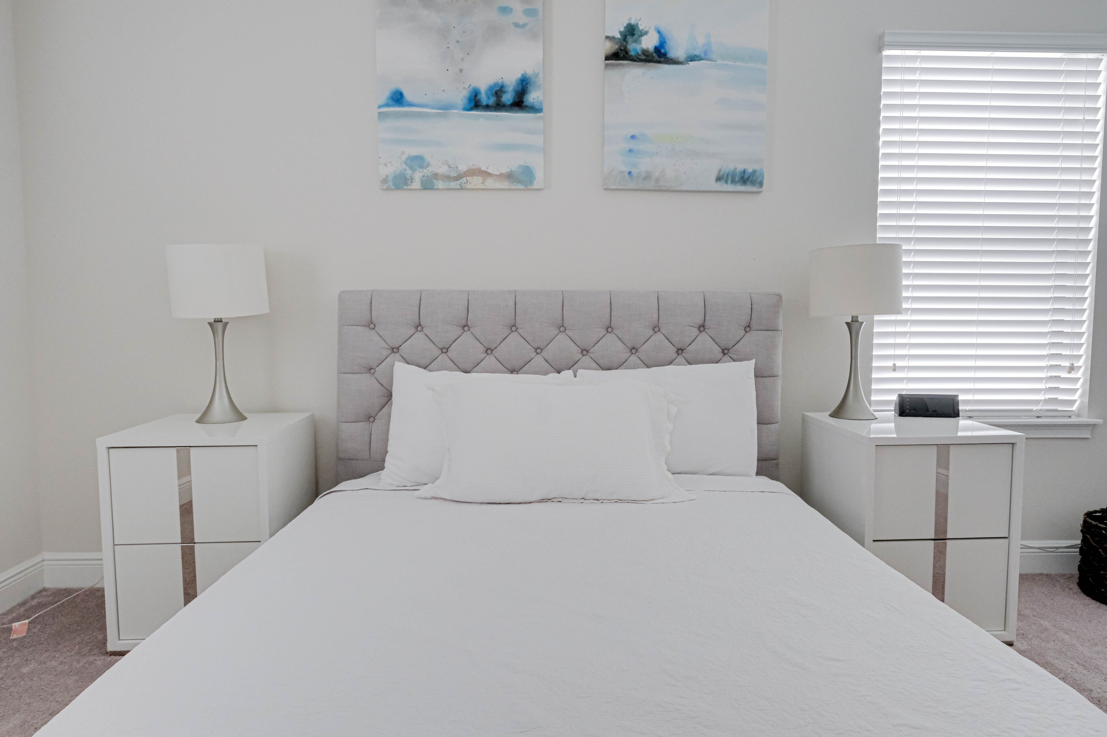 A bedroom with a large bed, two nightstands, and a window with blinds.