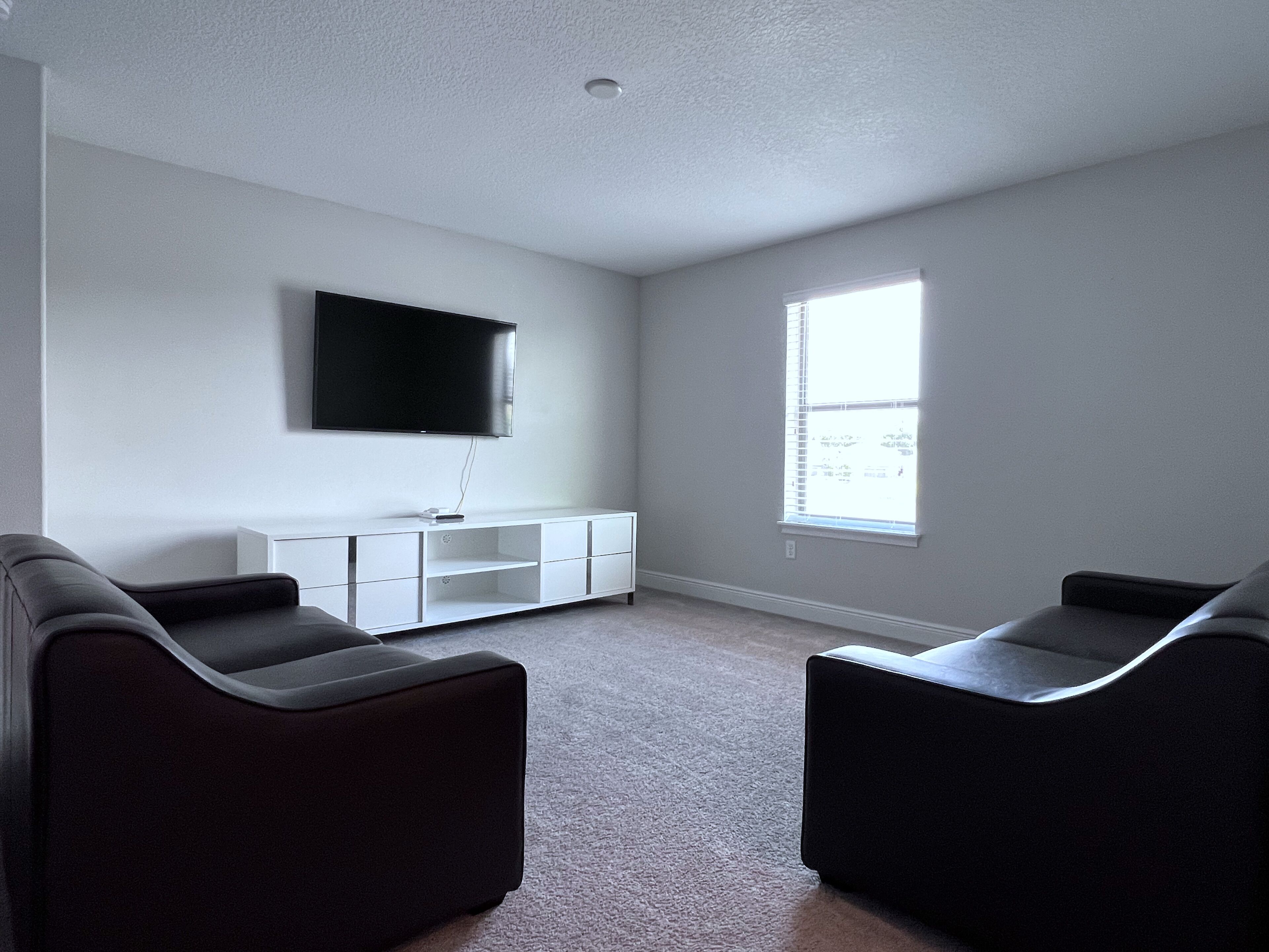 A modern living room with a flat-screen TV mounted on the wall, a white entertainment unit, and two black sofas.