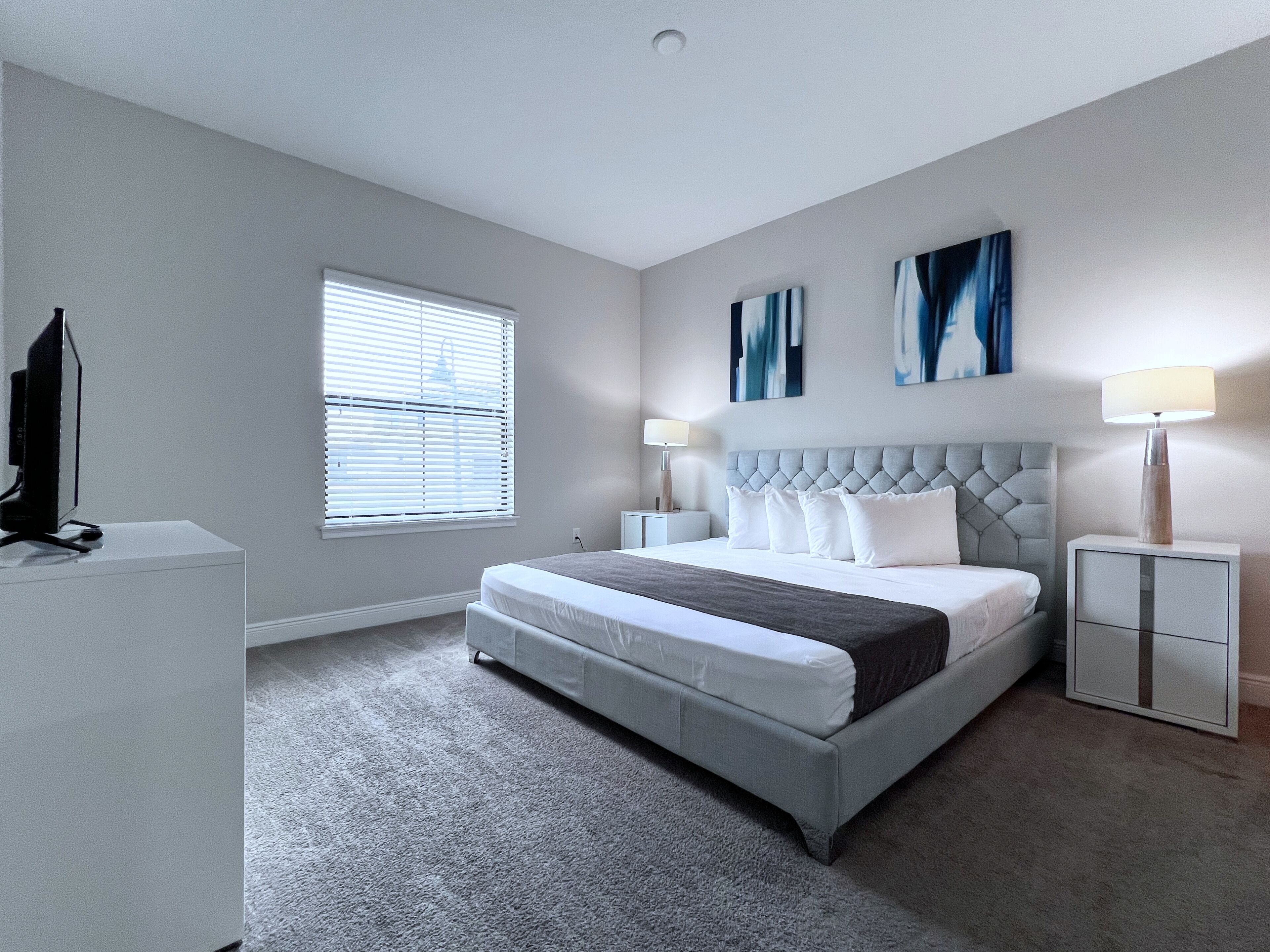 A modern bedroom with a large bed, two bedside tables, a TV, and artwork on the walls.