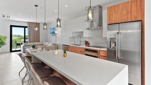 A modern kitchen with a large island, stainless steel appliances, pendant lighting, and a view to the outdoors.