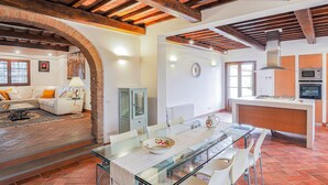 A spacious living area with a glass dining table, white chairs, a sofa, and a kitchen with modern appliances. - Villa in Certaldo ID 4125 (Certaldo)