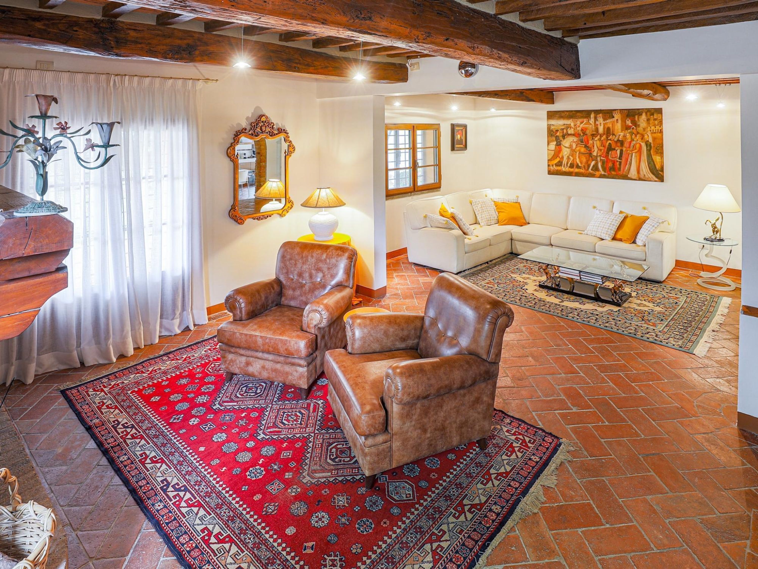 A spacious living room with a leather armchair, a patterned rug, and a white sofa with yellow cushions.