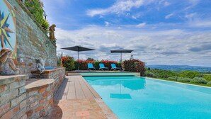 A swimming pool with a wooden deck, two umbrellas, and blue lounge chairs. - Villa in Certaldo ID 4125 (Certaldo)