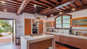 A modern kitchen with a central island, wooden beams, and a large window. - Villa in Certaldo ID 4125 (Certaldo)
