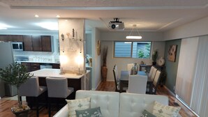 Una sala de estar moderna con un sofá blanco, un comedor con una mesa y sillas, y una cocina al fondo.