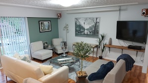 Una sala de estar con un sofá, sillones, una mesa de centro, un televisor y un cuadro en la pared.