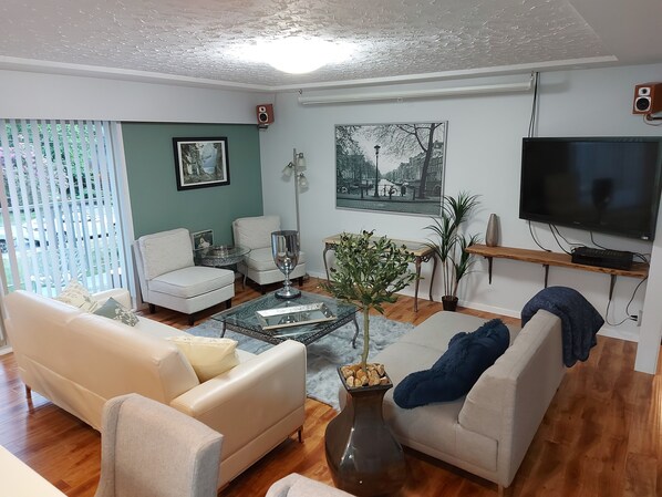 Uma sala de estar com sofá, poltronas, mesa de centro, televisão e um quadro na parede.