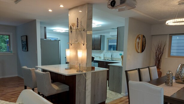 Una cocina moderna con una isla central, una zona de comedor con sillas blancas y un proyector instalado en el techo.