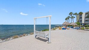 Une plage avec un fauteuil à bascule, des chaises longues et un bâtiment bordé de palmiers.