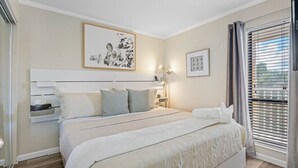 Une chambre à coucher avec un lit, des tables de chevet, une commode, un tableau encadré et une fenêtre avec des stores.