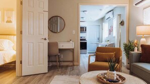A cozy living room with a round coffee table, a sofa, and a chair. A desk with a chair is in the background, and a kitchen area is visible through an open door. - Lamont 1 2bed Pet-Friendly Apt (Johnson City)